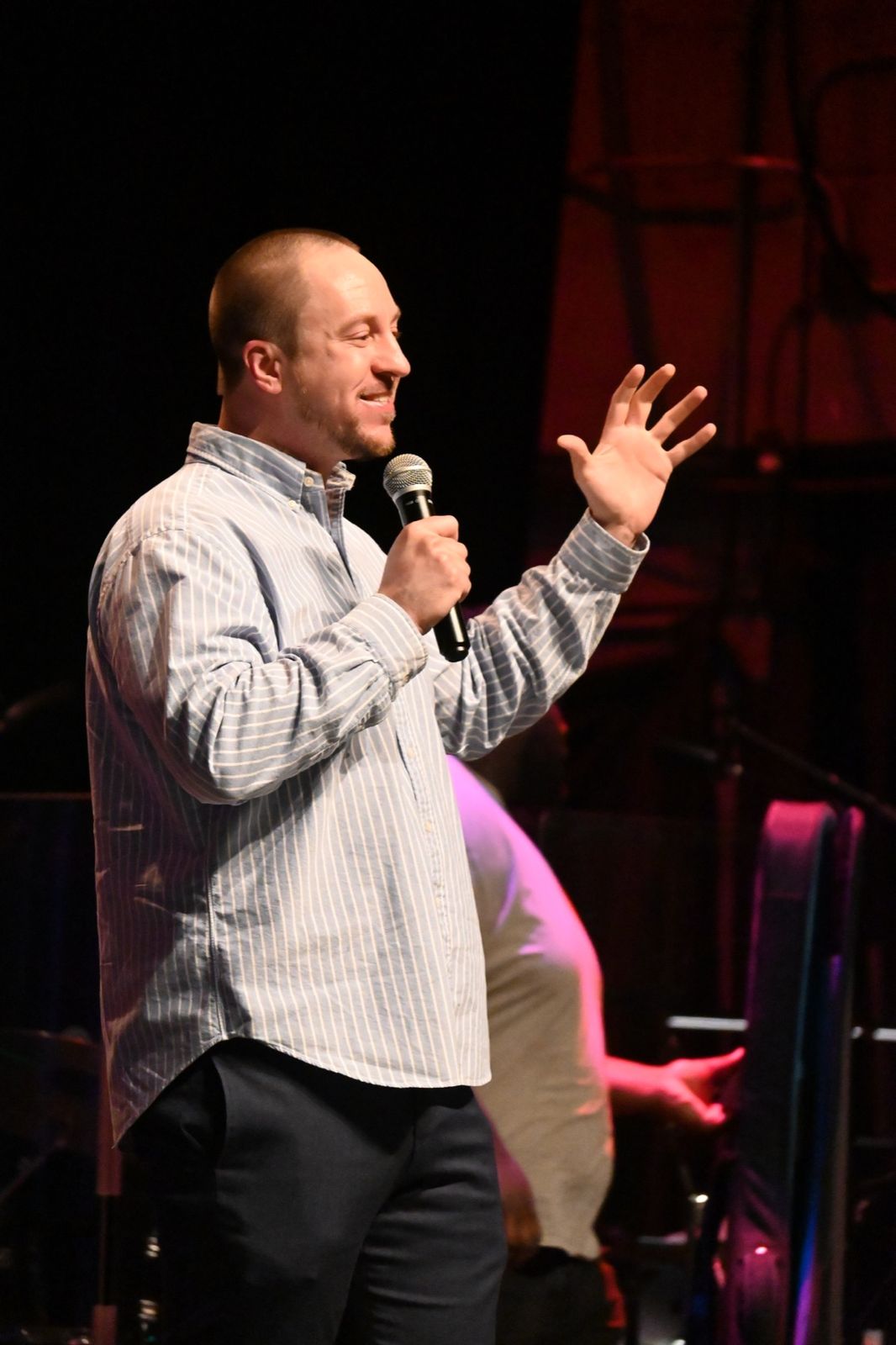 A speaker smiling and gesturing with a microphone on stage at an ICN gathering